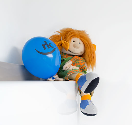 Eine Puppe mit einem Luftballon mit Logo drauf daneben